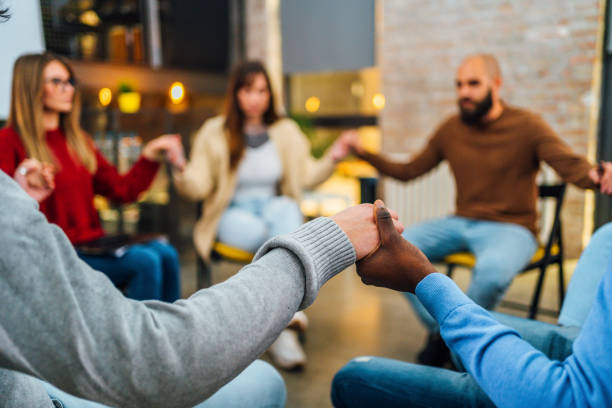 Group of people holding hands in support group therapy stock photo