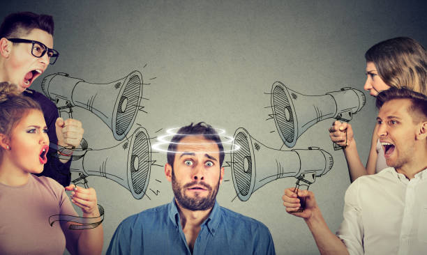 Group of people screaming in megaphones at scared guy stock photo