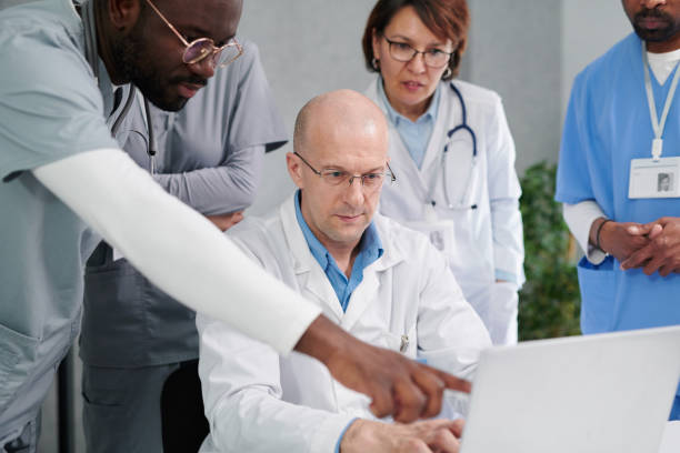 Group of physicians using laptop at work Multiethnic group of medical workers discussing disease together using laptop during consultation at office medical assistant online courses stock pictures, royalty-free photos & images