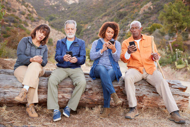 Group Of Senior Friends On Hike In Countryside Checking Mobiles Phones For Fear Of Missing Out Group Of Senior Friends On Hike In Countryside Checking Mobiles Phones For Fear Of Missing Out fomo photos stock pictures, royalty-free photos & images