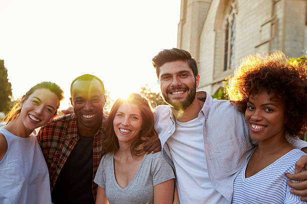 Group of smiling young adult friends embracing in the street Group of smiling young adult friends embracing in the street arm around stock pictures, royalty-free photos & images