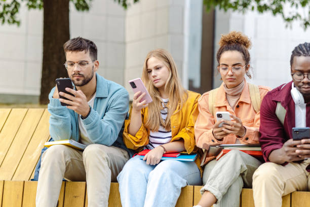 Group of students sitting together and using their smart phones Group of University students sitting on the bench and consuming internet content fomo photos stock pictures, royalty-free photos & images