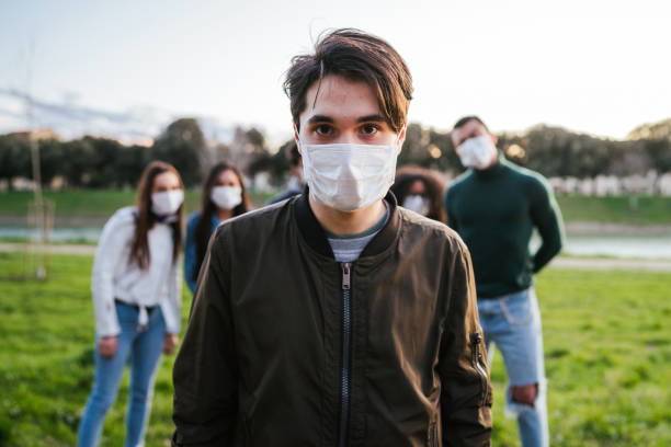 Group of teenagers friends at park wearing medical masks to protect from infections and diseases - Conceptual Coronavirus virus quarantine - Copy space - Multiracial people having fun together stock photo