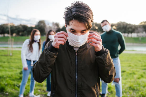 Group of teenagers friends at park wearing medical masks to protect from infections and diseases - Conceptual Coronavirus virus quarantine - Copy space - Multiracial people having fun together stock photo