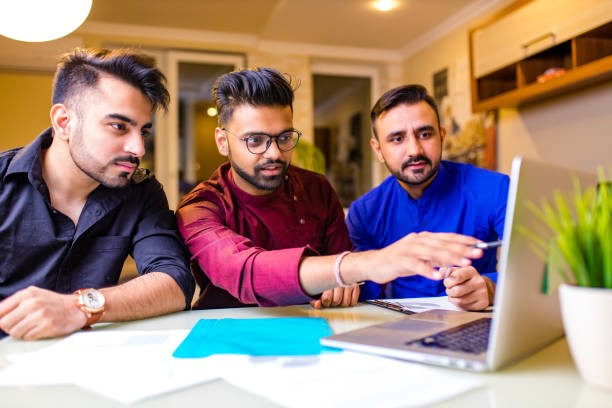 group of three indian students looking at laptop indoors stock photo