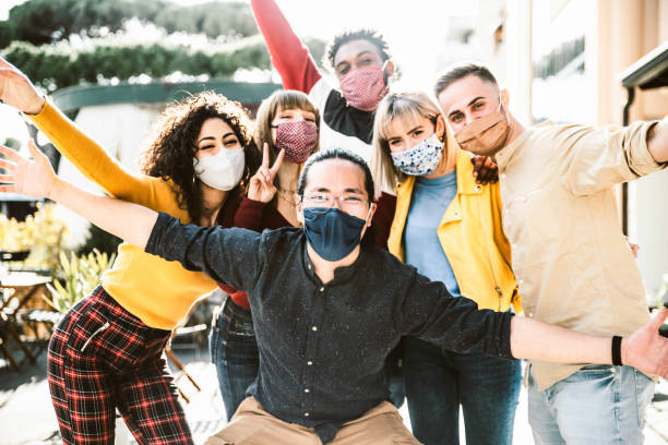 Group of tourists wearing protective face mask on city street smiling at camera - New normal concept with young people having fun on vacation - Reopening holidays concept stock photo