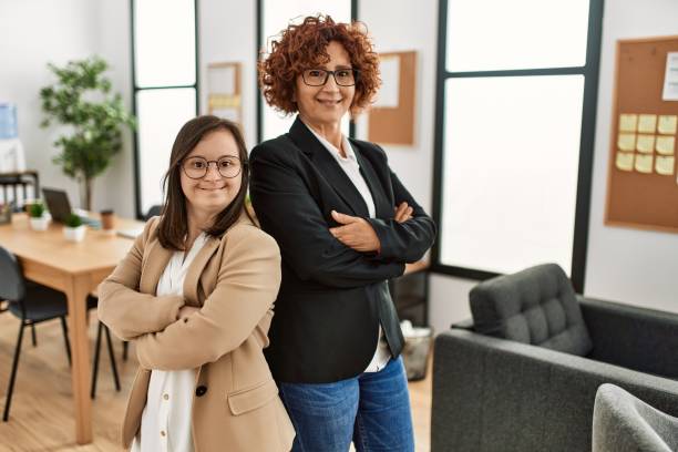 Group of two women working at the office. Mature woman and down syndrome girl working at inclusive teamwork. stock photo