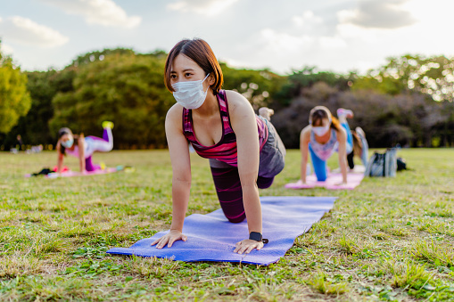 A group of women are wearing protective face masks and doing fitness sports training in nature.