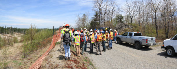 Group of workers and geologists in hardhats and high-visibility vests standing on road. SUDBURY, ONTARIO, CANADA - MAY 21 2009: Group of workers and geologists in hardhats and high visible vests inspecting site. View from the back. Gathering on dirt road. geologist stock pictures, royalty-free photos & images