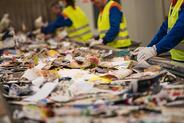 Workers sorting papers on factory assembly line for recycling at recycling plant.