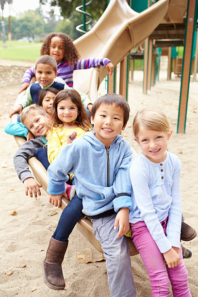 group of young children sitting on slide in playground - alleen kinderen stockfoto's en -beelden