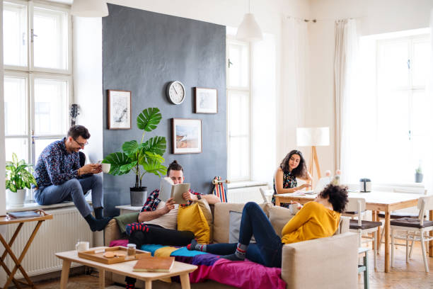 A group of young friends relaxing indoors, house sharing concept. A group of young cheerful friends relaxing indoors, house sharing concept. roommate stock pictures, royalty-free photos & images