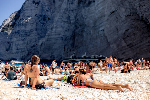 groep jonge vrienden zonnebaden op het strand van het scheepswrak van zakynthos - navagio beach stockfoto's en -beelden
