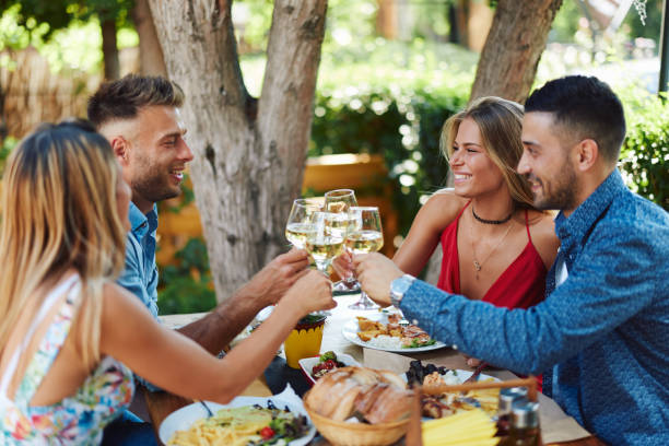 Group of young happy people toast with wine at lunch in restaurant during a sunny summer day stock photo