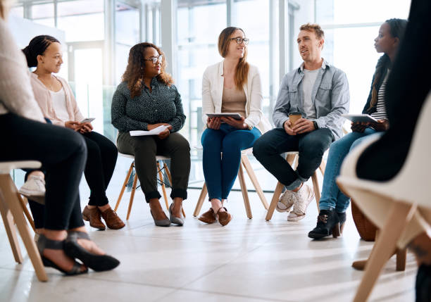Grow your network, grow your career Shot of a group of businesspeople sitting in a circle and having a meeting in a modern office group therapy stock pictures, royalty-free photos & images