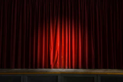 A spotlight shines on a grungy stage curtain in an abandoned school auditorium.