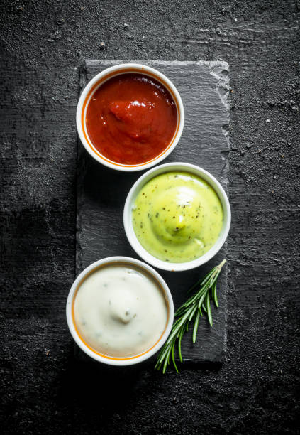 Guacomole sauce, tomato sauce and mayonnaise on a stone Board with rosemary. stock photo