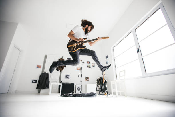 Guitarist jumping Young man jumping while playing electric guitar. Guitar head is changed, and it's not a copy of any existing guitar. Guitar head does not look like any other existing guitar head. rock musician stock pictures, royalty-free photos & images