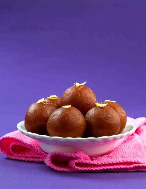 Gulab Jamun, Indian dessert topped with pistachio in white bowl with napkin stock photo