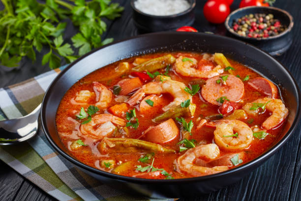gumbo with prawns, okra and sausage Delicious gumbo with prawns, baby okra and sausage in a bowl on a black table with napkin and silver spoon,  view from above, close-up gumbo stock pictures, royalty-free photos & images