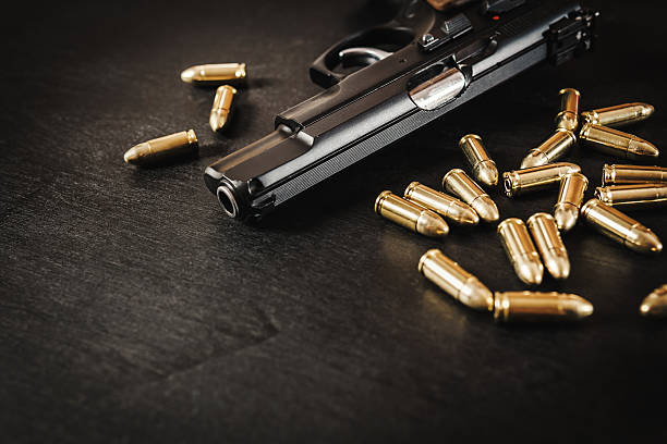 gun and bullets on the table black pistol and cartridges on a black wooden table weapon stock pictures, royalty-free photos & images