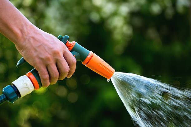 Gun water hose nozzle sprayer in use Gun water hose nozzle sprayer. Woman hand holding hose sprayer head watering garden. Shallow depth of field hand pump sprayer nozzles stock pictures, royalty-free photos & images