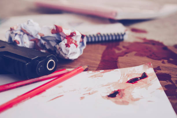gun with red flesh blood over the white paper with pencils, books stock photo