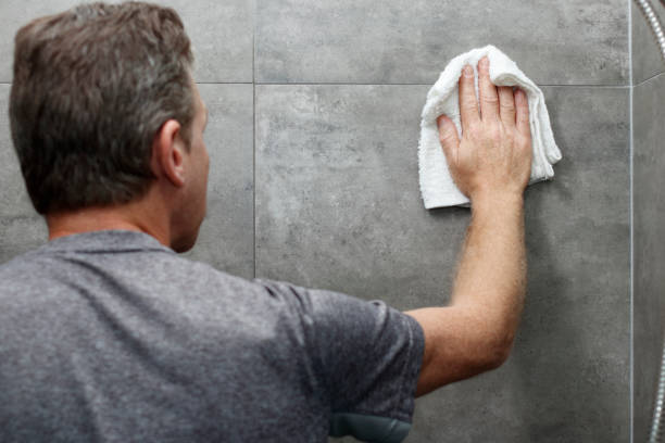 Guy Cleaning a Gray Tile Bathroom Shower Wall with a Rag stock photo