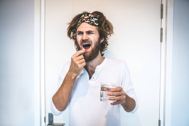 Guy drinking water and painkillers after a night of drinking alcohol. The day after hangover and intoxication. stock photo