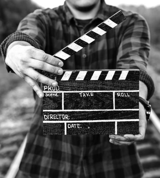 Guy is holding black clapperboard in hands. Man is directing and filming some amateur cinema movie. Rail trails on the background. Travel concept. Retro style. Black and white photo. Guy is holding black clapperboard in hands. Man is directing and filming some amateur cinema movie. Rail trails on the background. Travel concept. Retro style. Black and white photo. clapboard photos stock pictures, royalty-free photos & images