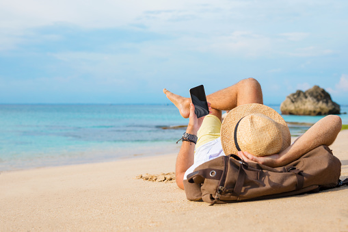Guy with smartphone lying on the beach. Unrecognisable young male using smartphone while relaxing at seaside