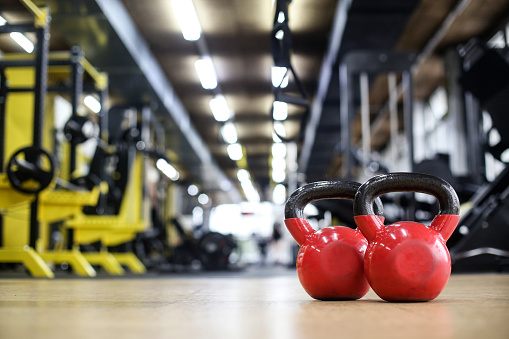 Close-up of two red kettlebell weights in a gym.
