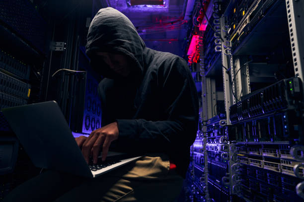 Hacker seated in server room launching cyberattack on laptop stock photo