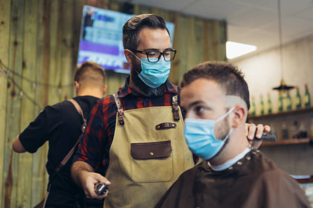 Hair cutting during pandemic. Young man have hair cutting at barber shop during pandemic isolation, they both wear protective equipment. stock photo