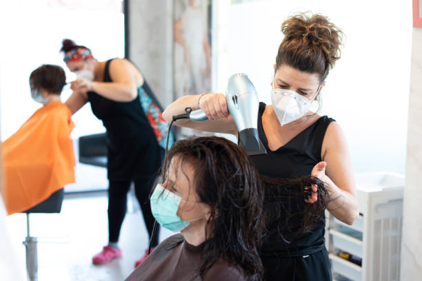 Hair dresser working with a face mask during coronavirus quarantine Working during covid-19 or coronavirus concept. A professional hairstylist cutting the hair to a client with a face mask. cutting hair stock pictures, royalty-free photos & images