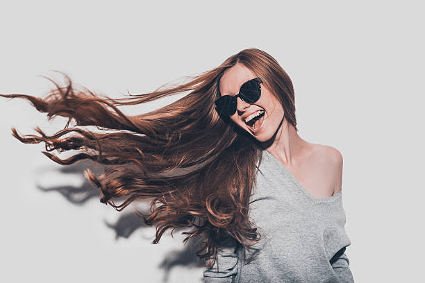 Hair like fire. Attractive young smiling woman in sunglasses and with tousled hair looking away while standing against grey background long stock pictures, royalty-free photos & images