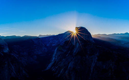 The sun starbursts from behind Half Dome in Yosemite National Park