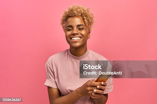 istock Half length shot of positive attractive female model with Afro haircut, feels good, uses smartphone device for entertainment and online chatting, surfers social network profile, uses free internet. 1326426267