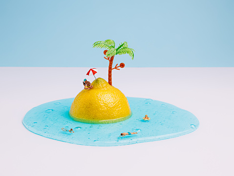 Half of a fresh lemon as a metaphor for an tropical island with a coconut tree and people swimming in the blue sea. Swimmers on vacation, summer creative art. Creative touristic holiday concept.