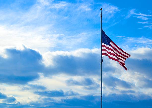 Half-Mast American Flag Against Blue Sky This half-mast American flag was captured against a perfect blue sky full of clouds. flag at half staff stock pictures, royalty-free photos & images