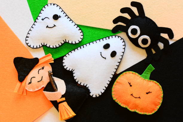 Halloween cute felt ornament decor. Small witch with broom, pumpkin head, two ghosts, spider. Halloween toys crafts on colored felt pieces. Simple kids sewing crafts concept. Top view stock photo