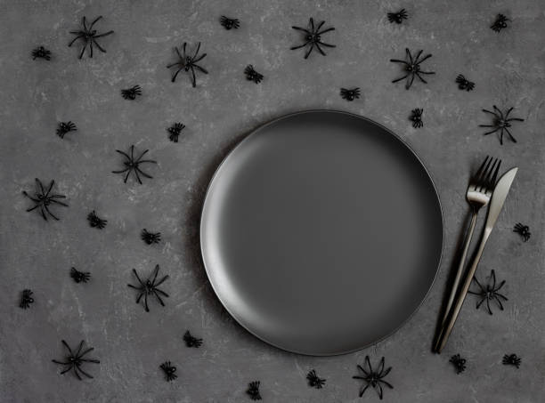 Halloween table setting with black crockery and spiders on dark gray background. Empty black plate for design. Copy space, top view, flat lay. stock photo