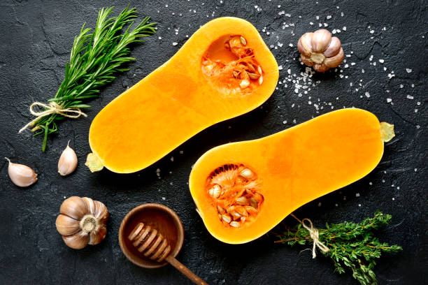 Halves of raw organic butternut squash with spices and ingredients for making Halves of raw organic butternut squash with spices and ingredients for making on a black slate, stone or concrete background.Top view. squash vegetable stock pictures, royalty-free photos & images