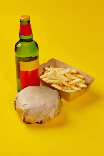 Hamburger in paper wrapping, fries in carton box and bottle of drink on yellow background Fresh hamburger in paper wrapping, crispy French fries in carton box and glass bottle of drink isolated on yellow background. Set from fast food restaurant menu. Popular snacks concept burger wrapped in paper stock pictures, royalty-free photos & images