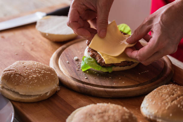 hamburger préparant, feuille de fromage mou mis sur le pain de hamburger, plan rapproché - faire part photos et images de collection