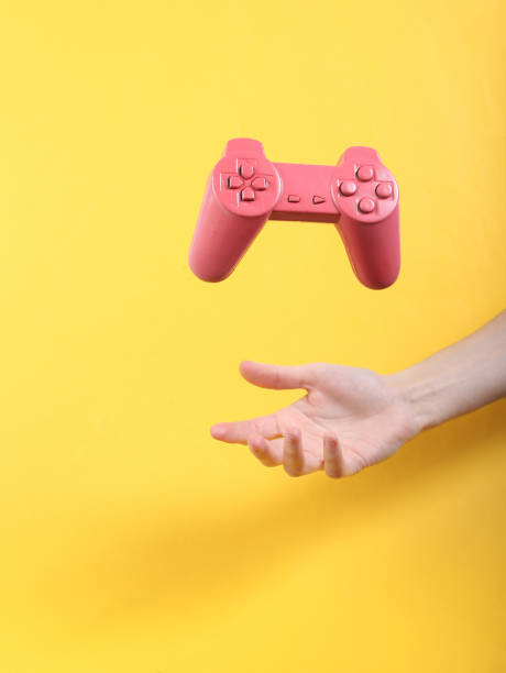 Hand and Levitating pink gamepad on yellow background. Minimalistic still life. Concept art. Video game stock photo