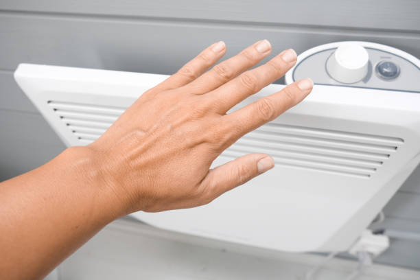 A hand checking temperature of heating convector on the wall, air heating the house in fall and winter stock photo
