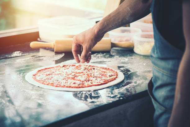 hand Chef preparing spread cheese on pizza on marble table stock photo