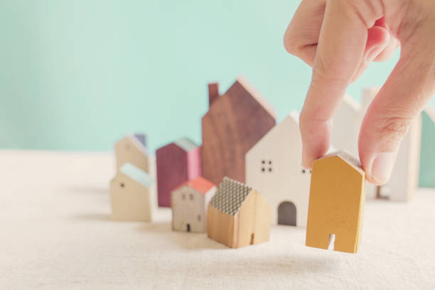 Hand choosing yellow miniature house, searching right property in high demand housing boom, making decision on home investment concept stock photo
