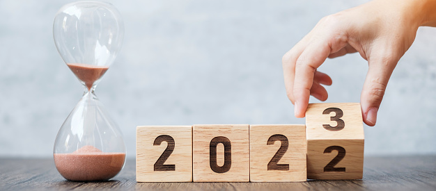 hand flip block 2022 to 2023 text with hourglass on table. Resolution, time, plan, goal, motivation, reboot, countdown  and New Year holiday concepts